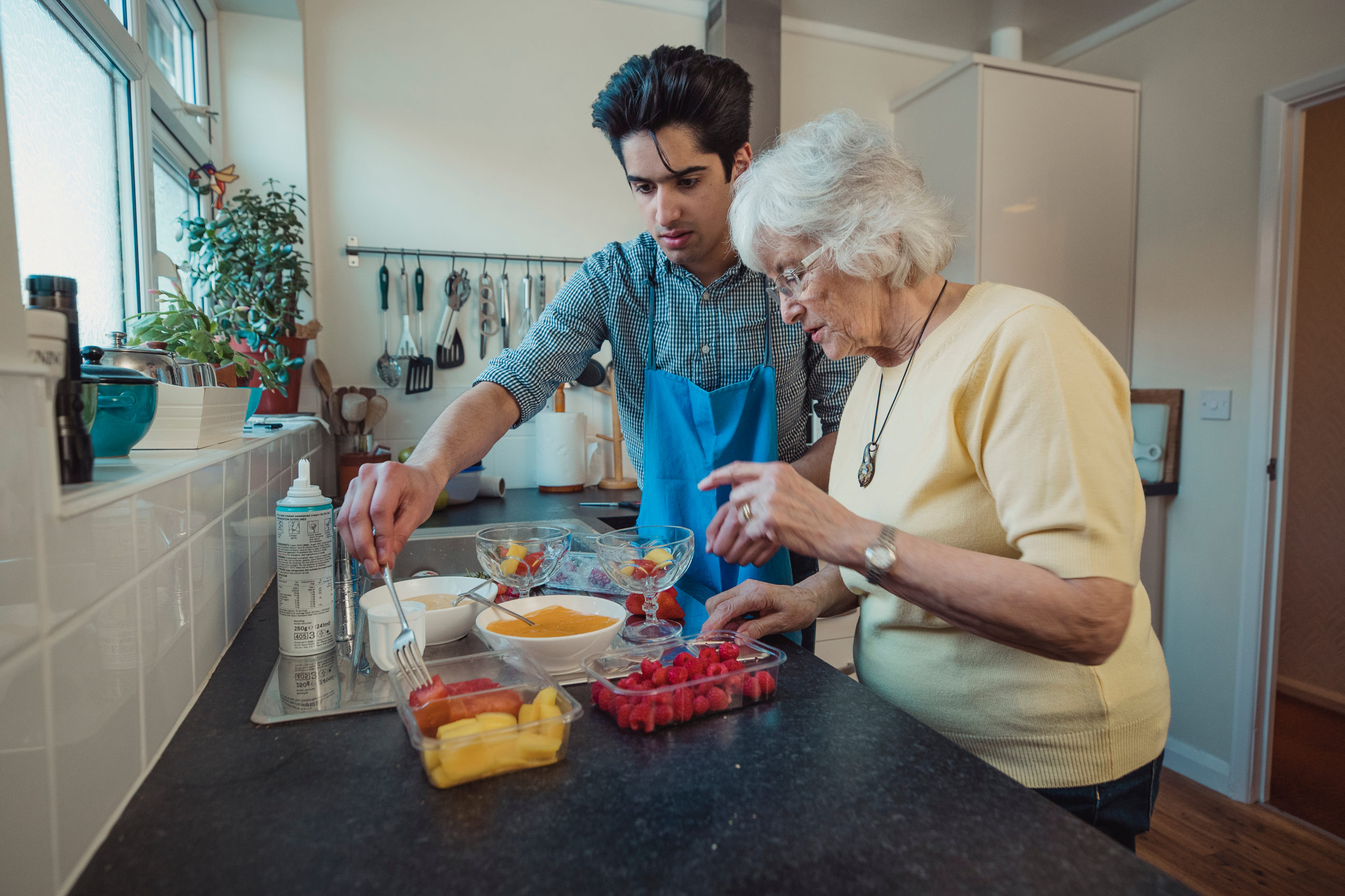 Teenage boy making fruit compote with his grandmother in the kitchen of her home.